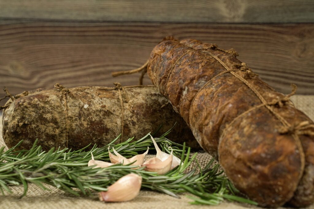 Immagine del Salame Affumicato allAglio un salume caratterizzato da una superficie scura e affumicata Il salame è aromatizzato con aglio offrendo un sapore robusto e intenso